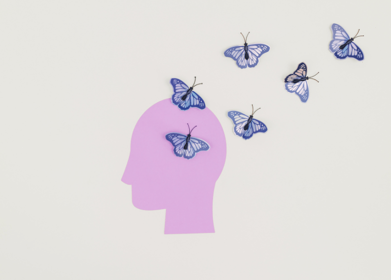Purple paper cutout of a human head with blue butterflies flying out