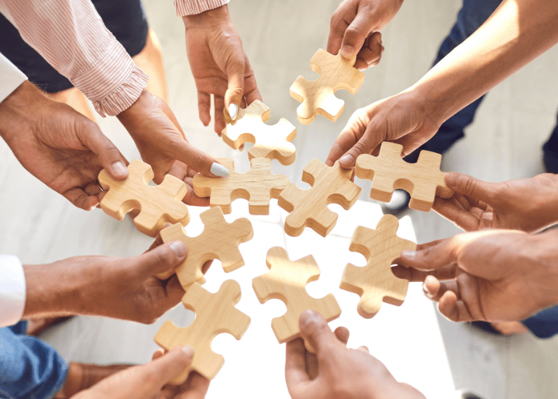 Employees holding wooden puzzle pieces together, representing collaboration, teamwork and employee experience.