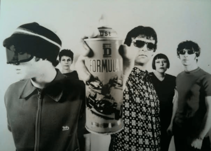 Black-and-white photo of the 1990s indie band Formula One, with five band members posing around a large Formula One trophy.