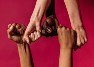 Diverse group of four people joining fists together, symbolising teamwork, collaboration and inclusion.